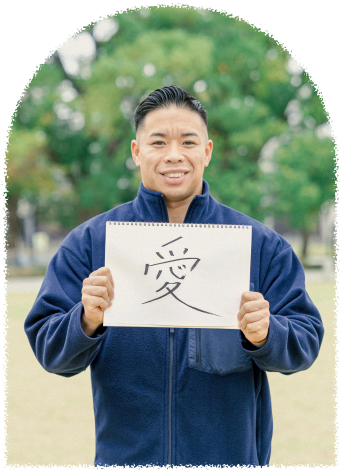 笑顔の男性スタッフがスケッチブックを掲げている。大切にしたい信念である「愛」という文字が書かれている