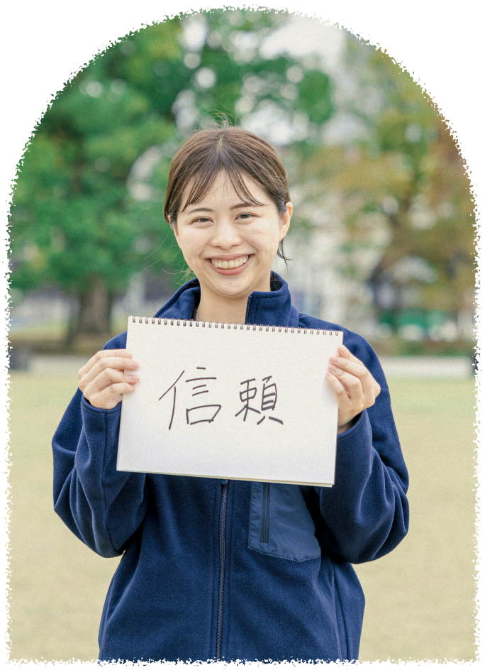 笑顔の女性スタッフがスケッチブックを掲げている。大切にしたい信念である「信頼」という文字が書かれている
