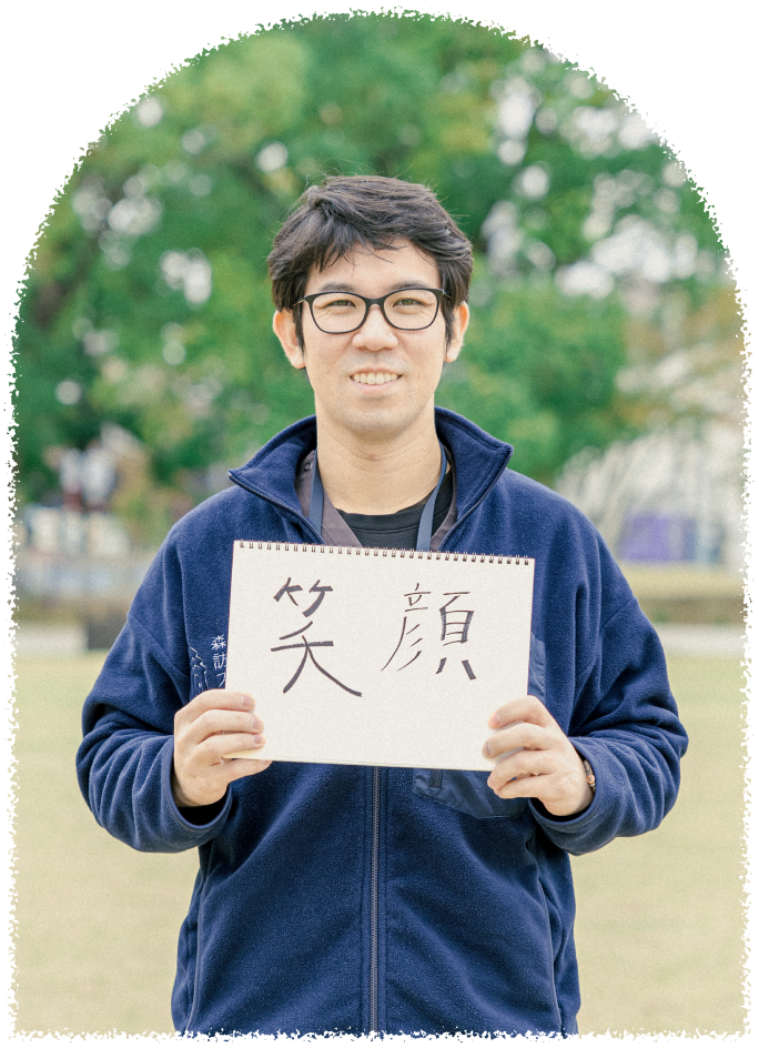 笑顔の男性スタッフがスケッチブックを掲げている。大切にしたい信念である「笑顔」という文字が書かれている