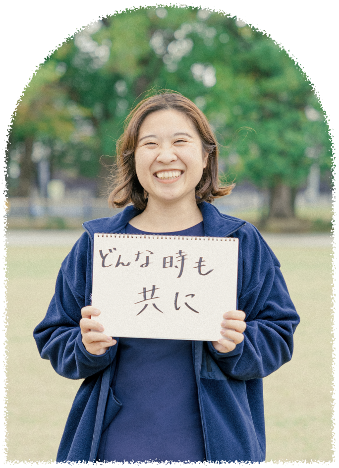 笑顔の女性スタッフがスケッチブックを掲げている。大切にしたい信念である「どんな時も共に」という文字が書かれている