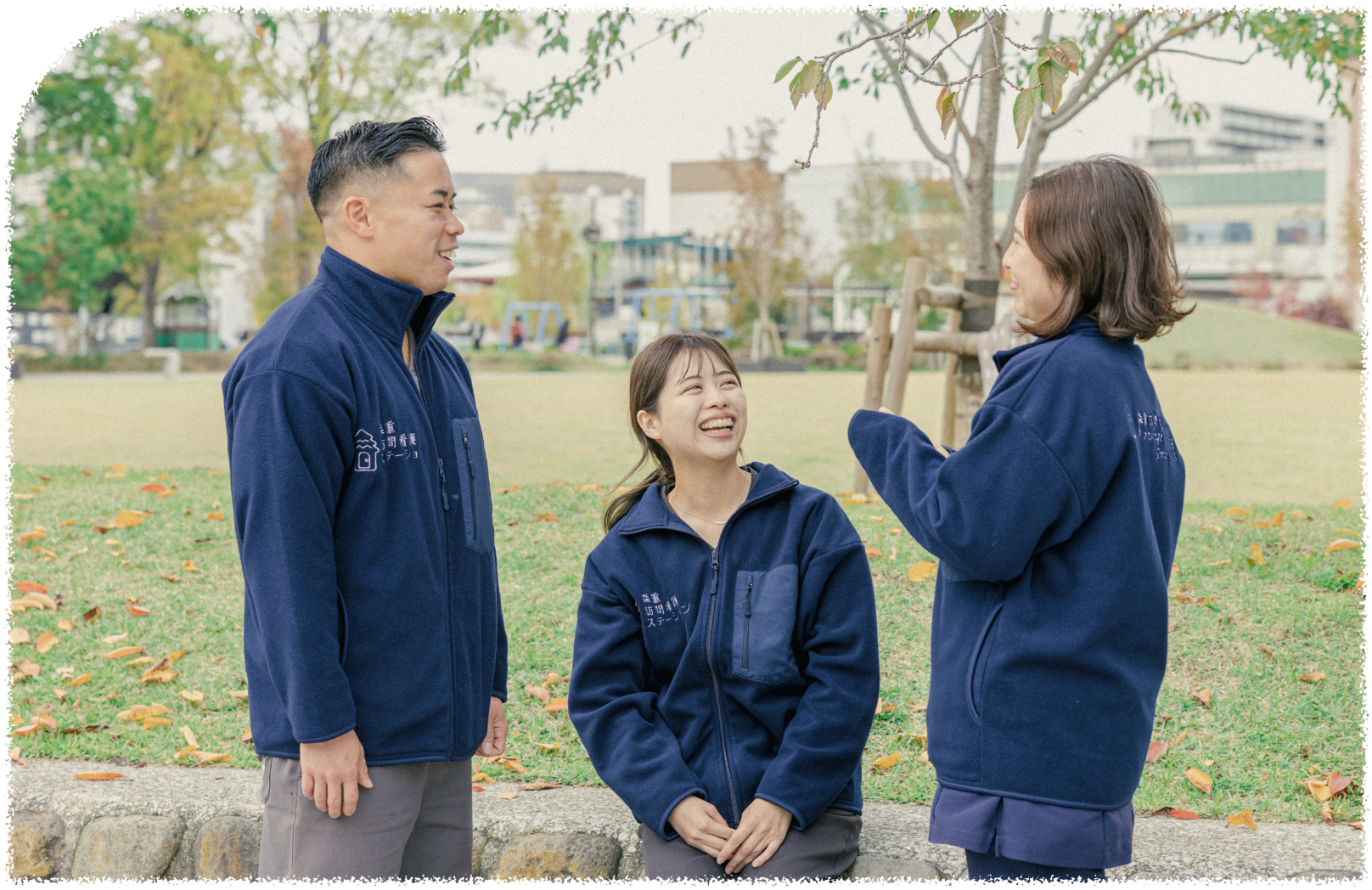 笑顔の男性スタッフ一名と女性スタッフ二名が公園で楽しそうに会話している