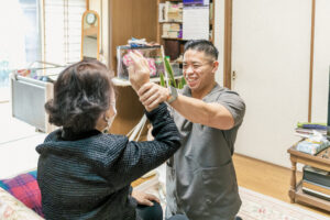 笑顔の男性スタッフが高齢女性の右上を上げてストレッチを行っている