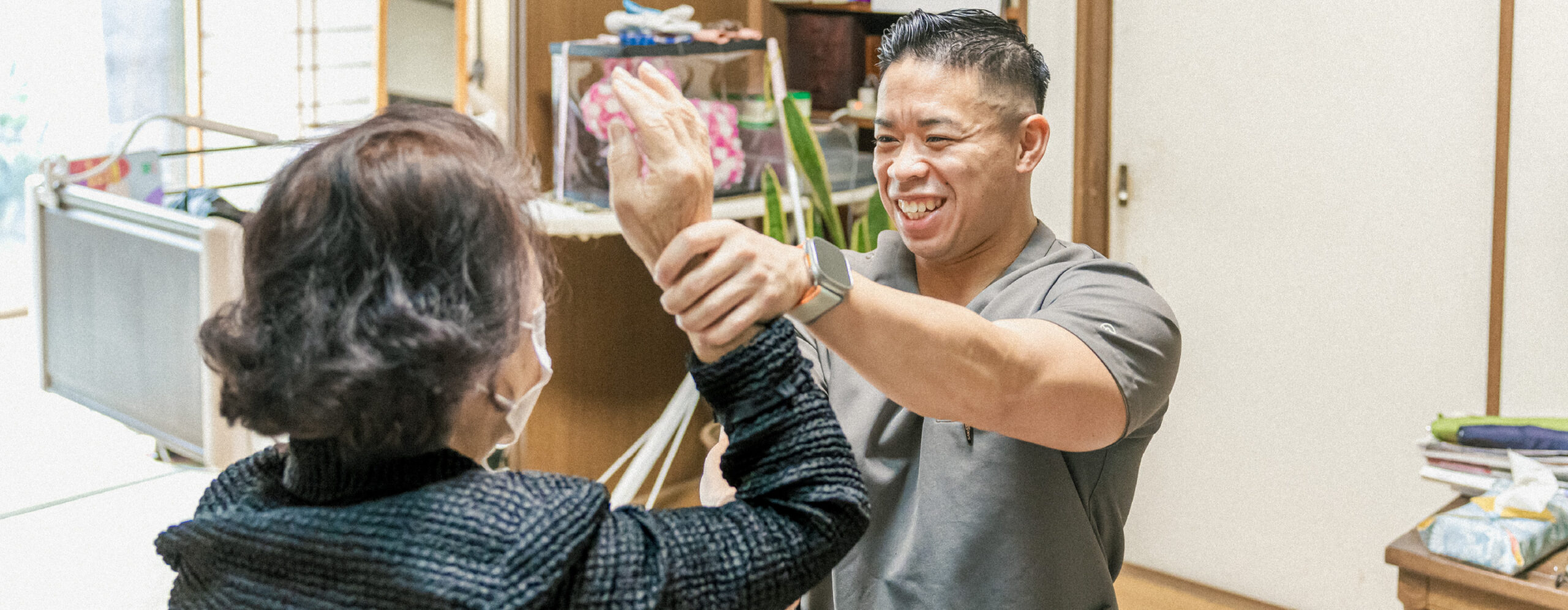 笑顔の男性スタッフが高齢女性の右上を上げてストレッチを行っている
