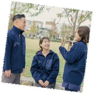 笑顔の男性スタッフ一名と女性スタッフ二名が公園で楽しそうに会話している