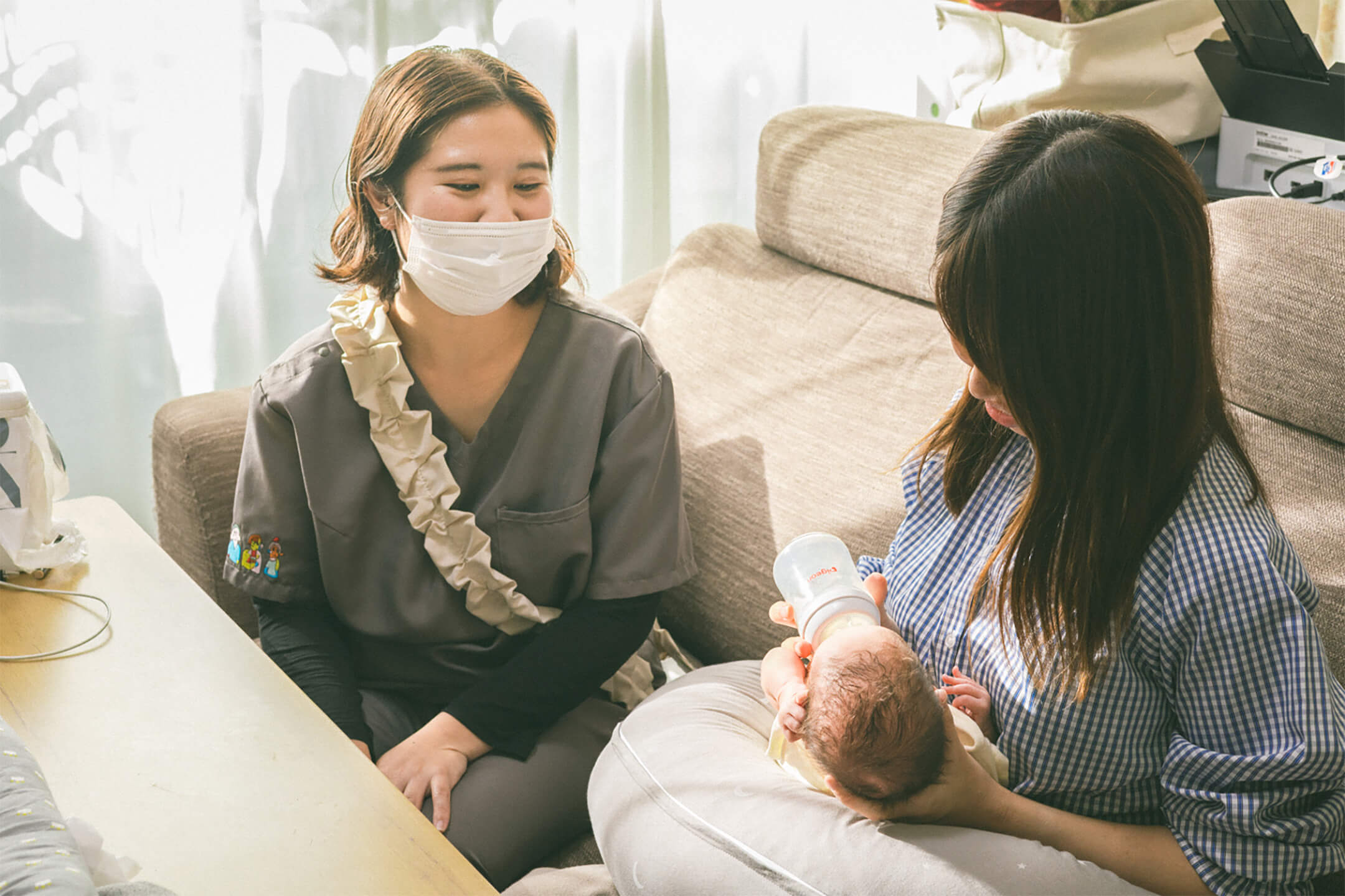 お母さんが赤ちゃんにミルクをあげている様子。女性スタッフが見守っている