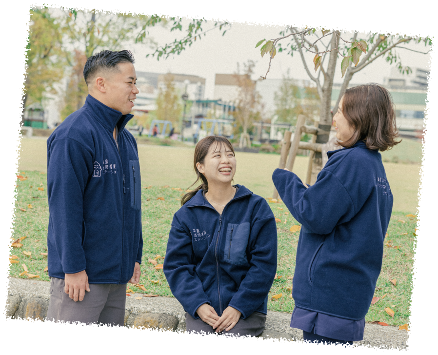笑顔の男性スタッフ一名と女性スタッフ二名が公園で楽しそうに会話している